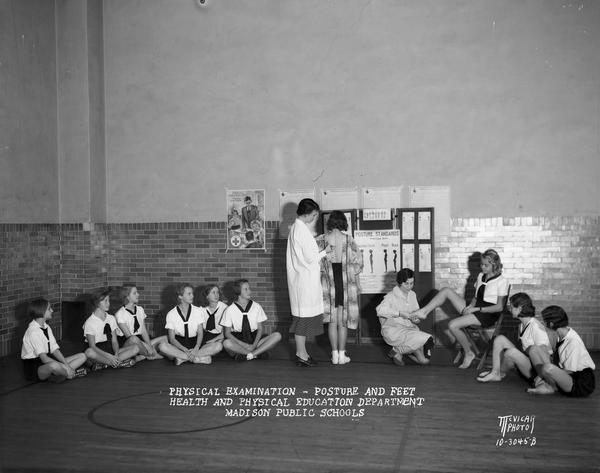 Two women from the Health and Physical Education Department examining the posture and feet of Emerson School girls dressed in gym uniforms.