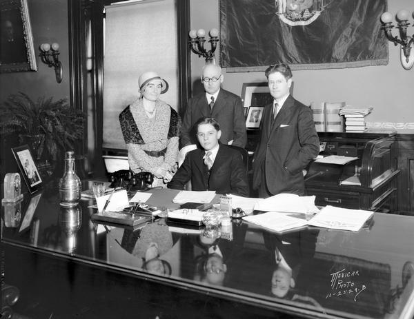 Norman Clapp, Appleton High School student, sitting in the governor's chair, represents Wisconsin in the around-the-world telephone conversation held in conjunction with International Good Will Day. Others left to right are Blanche McCarthy, president Wisconsin Teachers' Association; John Callahan, state superintendent of public instruction; and Governor Philip F. La Follette.