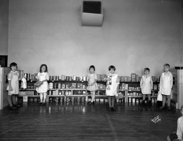 Six kindergarten children wearing aprons stand in front of a classroom grocery display at Lapham School, 1436 E. Dayton Street.