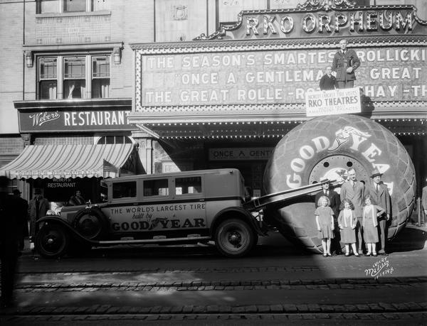 Group of people, including dwarfs and midgets, posing with "the worlds largest tire" in front of the RKO Orpheum Theatre as part of a promotion for Goodyear Tires. "Once a Gentleman" is on the marquee.
