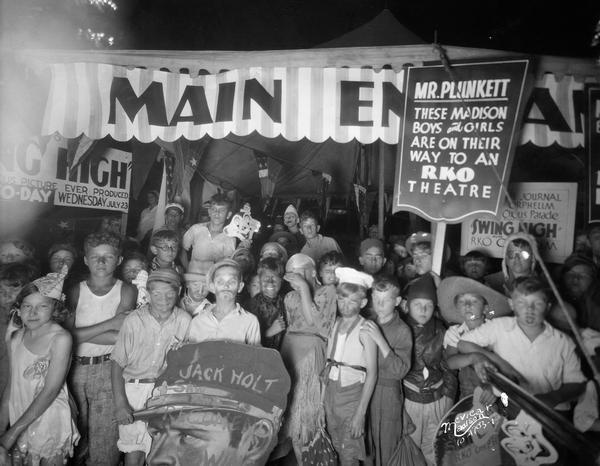 A crowd of children, some in costume, gather at the Orpheum Theatre entrance behind a caricature labeled "Jack Holt" during a promotion for the film, "Swing High."