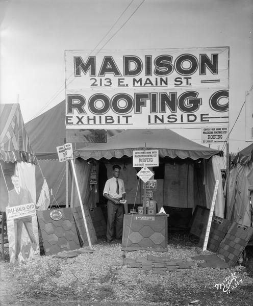 A man standing in the Madison Roofing Company booth at the Dane County Fair displaying various samples of roofing materials.