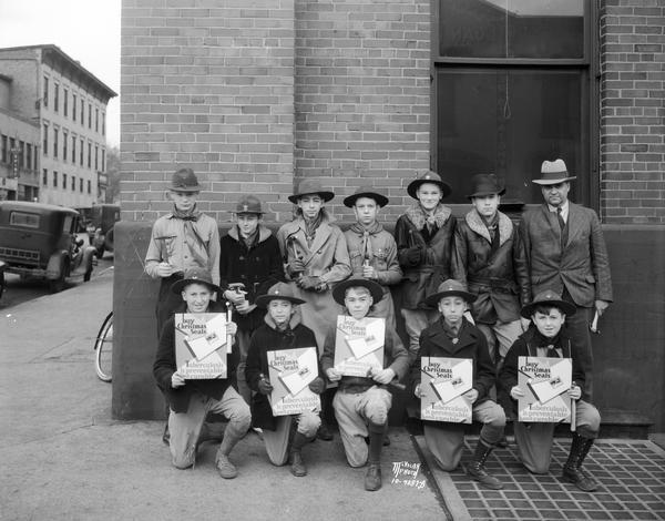 A group portrait of Boy Scouts and adult leaders armed with tacks, hammers and posters to promote the sale of Christmas Seals.