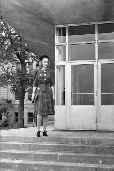 Manchester's Department Store coed model, wearing dress, hat and purse, posing beside the Memorial Union on University of Wisconsin-Madison campus.