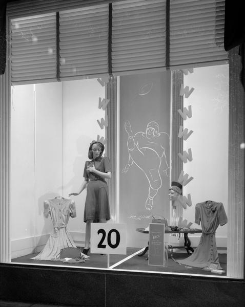Manchester's, Inc., 20 Yard Line window with mannequin wearing a dress. Two more dresses and other items are displayed, with a sign that reads, "You'll get a kick out of wearing these to the game." There is a drawing of a football kicker in the background.