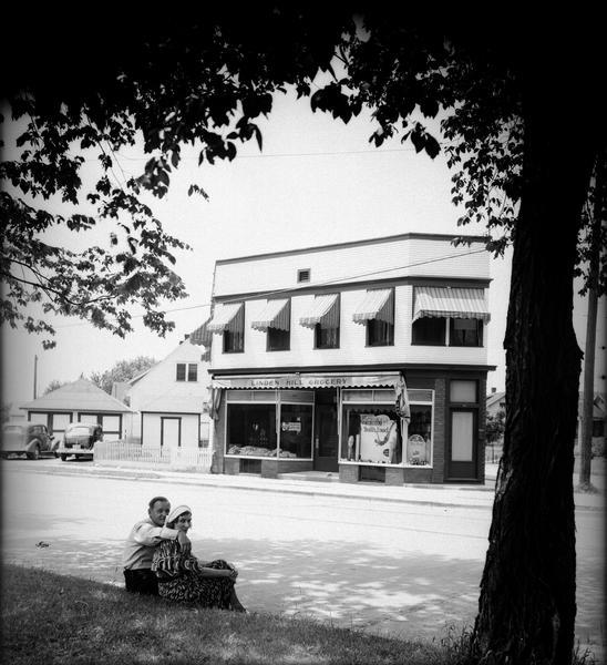 Linden Hill Grocery Store, 36 South Fair Oaks Avenue. Anton "Tony" Lazarz and his wife Bernice, owners of the store, are sitting on the curb in the foreground, which is across the street from the store.