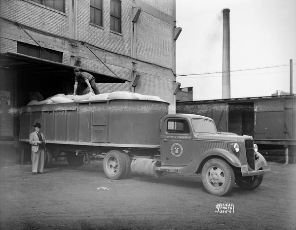Three men loading seed sacks into Green & Company Ford semi-trailer truck at Olds Seed Co. loading dock, 722 Williamson Street. Sign on truck reads: "Green seeds for green fields." The company was located in Evansville, Wis.
