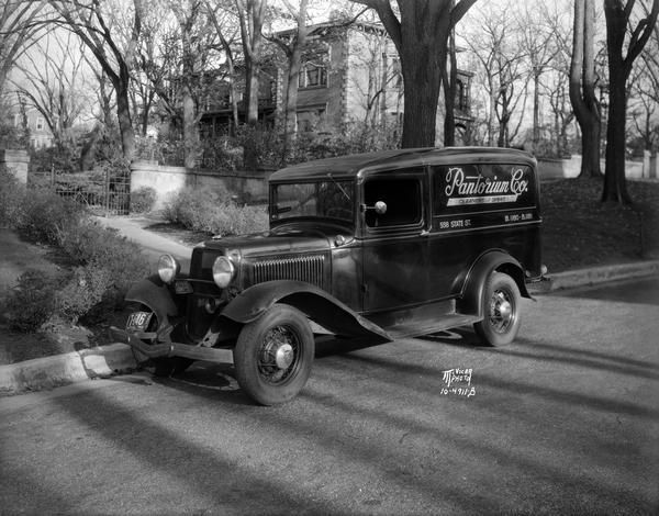 Delivery truck for Pantorium Cleaners, 558 State Street, with Hanks mansion, located at 525 Wisconsin Avenue, in the background among trees.