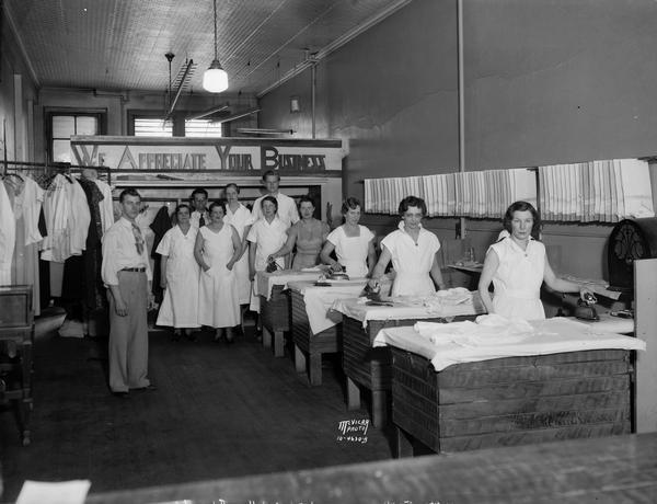 Interior of the Varsity Hand Laundry, located at 527 State Street. There are four women ironing, and several workers are standing behind them. A sign in the background reads: "We Appreciate Your Business."