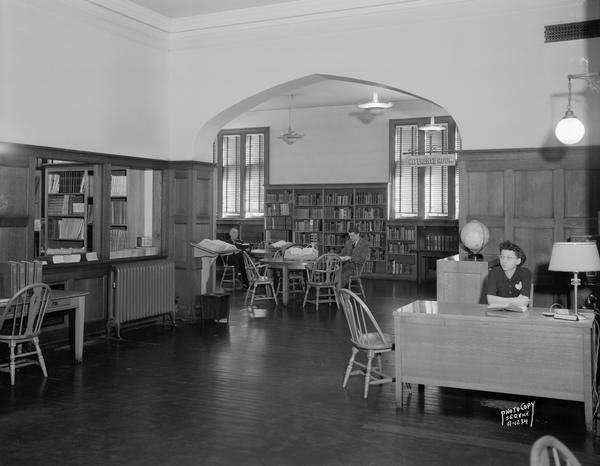 Interior of Madison Public Library, 206 North Carroll Street. The view shows the Reference Room, Information Desk, one librarian and two patrons.