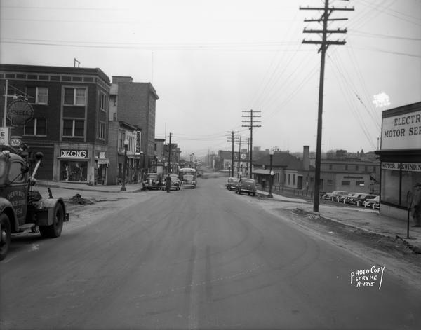 View down middle of East Wilson Street at the center of South Hancock looking Northeast, taken at site of Reynolds Bus accident. Businesses shown include Dizon Men's Clothing at 402 East Wilson Street, Krehl's Drugstore at 408 East Wilson Street, the Cardinal Hotel at 416-18 East Wilson Street, the Milwaukee Road Franklin Street station at 501 East Wilson Street, and Electric Motor Service at 323 East Wilson Street.