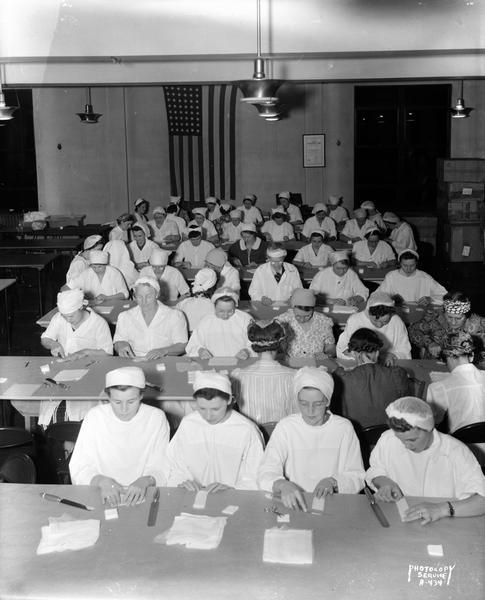 Large group of Red Cross Workers seated at tables, preparing surgical dressings in the assembly room at the American Federation of State, County and Local Employees Building, 448 West Washington Avenue.