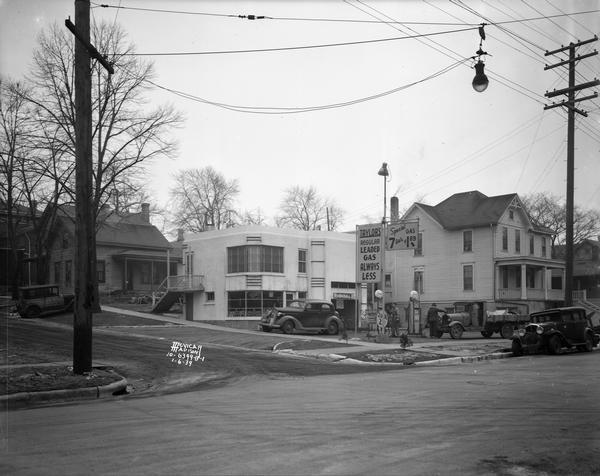 View from street towards two men filling the gas tanks of a car and truck at Jack D. Taylor's Super Service Station, 751-753 Williamson Street. This Art Deco style building is located at the corner of Williamson and Livingston Street.