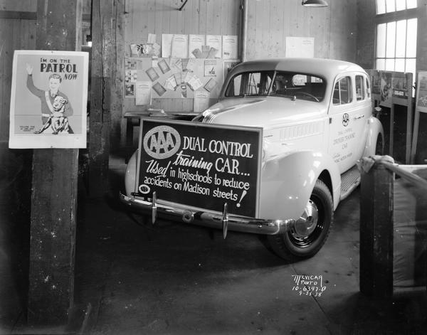 Pontiac automobile with sign "AAA dual control training car." The car was used in high schools to reduce accidents on Madison streets and is on display here at the East Side Business Men's Association Fall Festival. On the wall is a poster about safety patrol activities.
