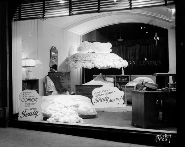 Display window at Leath Furniture Company, 117-119 State Street. Features Sealy mattresses in bedroom setting, soldier sleeping in a twin bed dreaming of a woman pictured on top of a Sealy mattress floating on a cloud. Sign states: "Home again! Dream again! Sealy again!"
