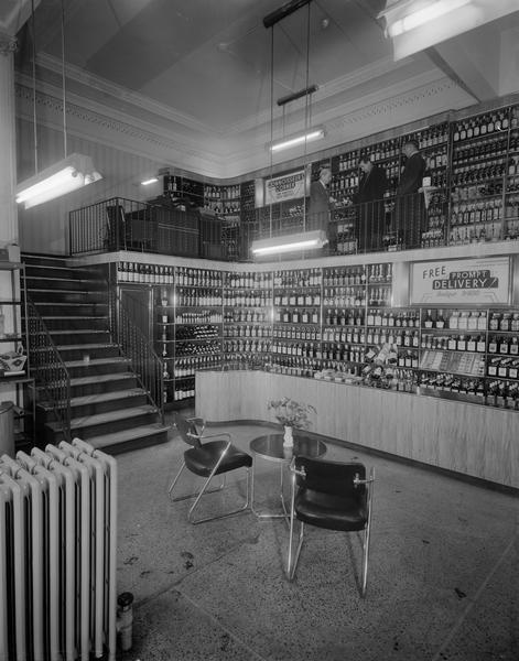 Interior view of Park Hotel Liquor Shop, 22 South Carroll Street, with Art Deco table and chairs and three men standing on the balcony in the "Connoisseur's Corner."