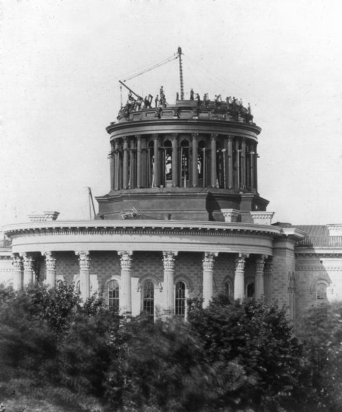 The second Wisconsin State Capitol dome under construction, showing the workmen and the equipment they used to hoist construction materials into place.