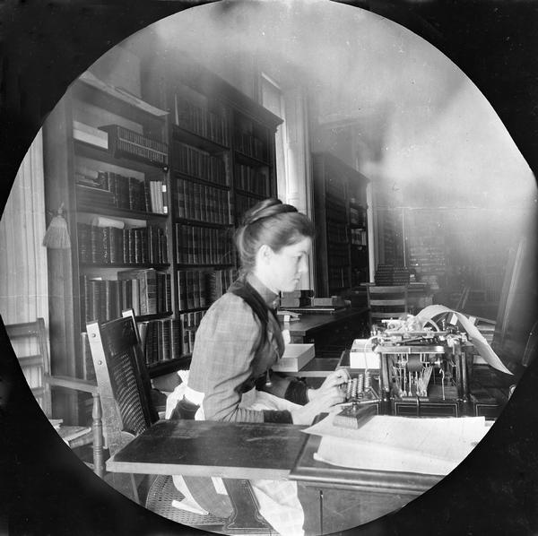 Emma Hawley, a Historical Society librarian, at her desk in the South Wing of the third Wisconsin State Capitol. After the Society purchased its first typewriter, Miss Hawley invented a device to accommodate catalog cards. Leaning forward in a chair that must have been uncomfortable for typing, she also permits us to better see the Eastlake style of her cane chair. This photograph was taken by Reuben Gold Thwaites, secretary of the Historical Society and an avid amateur photographer, using his new round-format Kodak 2 camera.