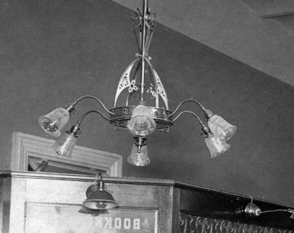 Detail of photograph of the office of the state treasurer, enlarged to show a typical lighting fixture from the third Wisconsin State Capitol. As originally installed, the chandelier was lit by gas, but the down-turned shades indicate that the fixture had been wired for electricity. By 1904 the Capitol had been wired for electricity, but two gas fixtures continued to be used at night in order to save money-a foolish economy.