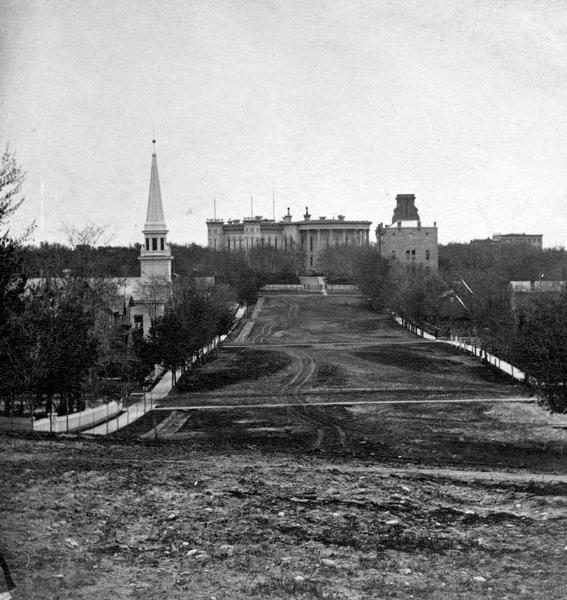 View from unpaved Wisconsin Avenue looking east toward the third Wisconsin State Capitol sometime prior to the completion of the dome (1869). The portion of the building seen here was designed by August Kutzbock and Samuel H. Donnel. Their dome was rejected, however, and Stephen V. Shipman designed the dome that was constructed.