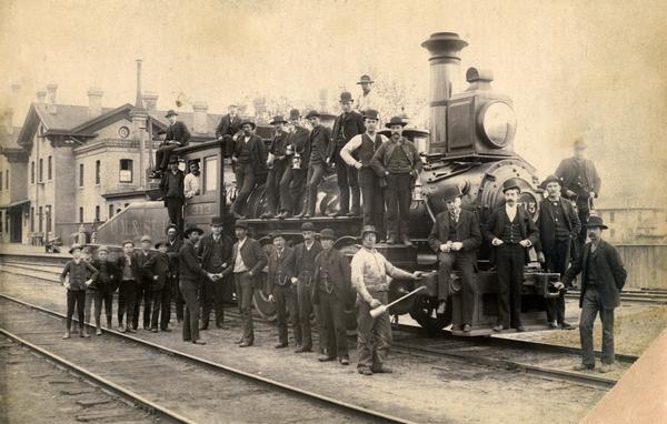 A group of men and boys posed around Chicago, Milwaukee & St. Paul Railway locomotive # 313, a switch engine. The Fox House is in the background.