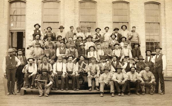 Group portrait of Chicago, Milwaukee & St. Paul Railway employees taken outside the railroad's Milwaukee shop. Most of the men appear to be blue collar workers. A few are holding the equipment with which they worked.
