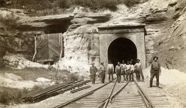 View down railroad tracks towards a group of construction workers posed near the east portal of the railroad tunnel near Tunnel City.