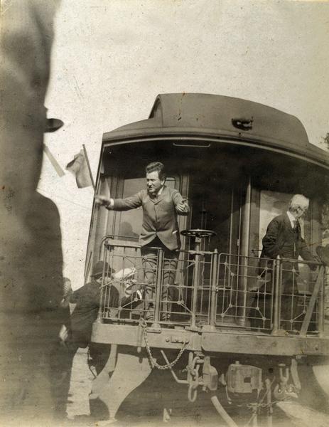 Robert M. La Follette, Sr., waving a flag from the back of a train as he campaigns for governor.