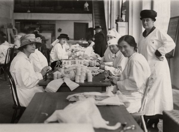 Red Cross volunteers preparing bandages at a Red Cross office in New York City. The woman standing on the right, who is supervising the work, is Mrs. Belmont Tiffany. The photograph is undated but the original caption indicates that it was taken before the American declaration of war.