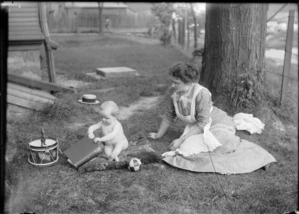 Beatrice C. Gesell and Gerhard Gesell, Jr. play out-of-doors.  While mother watches the baby sits on a pillow playing with a volume titled "Educational Problems."  Also pictured are a toy elf, a drum and a ball.
The picture being taken in Ridgeway is not confirmed.