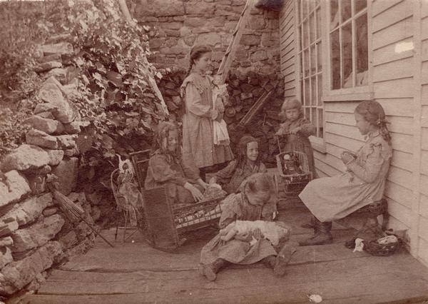 Six young girls playing with dolls on a porch.
