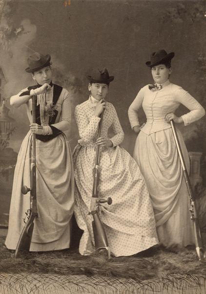 Studio portrait in front of a painted backdrop of Emma Protz, an unidentified woman (likely Julia Protz), and Clara Tester posing with "schuetzen-rifles." The Alma Schuetzenverein was a target shooting society organized on the same basis as those found in Switzerland at the time.