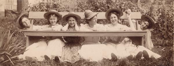 Six young women posing playfully beneath a bench.