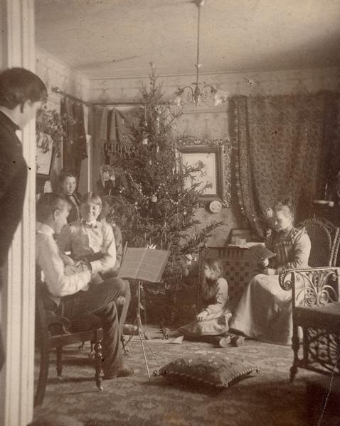 A family sits around a Christmas tree playing music and singing.