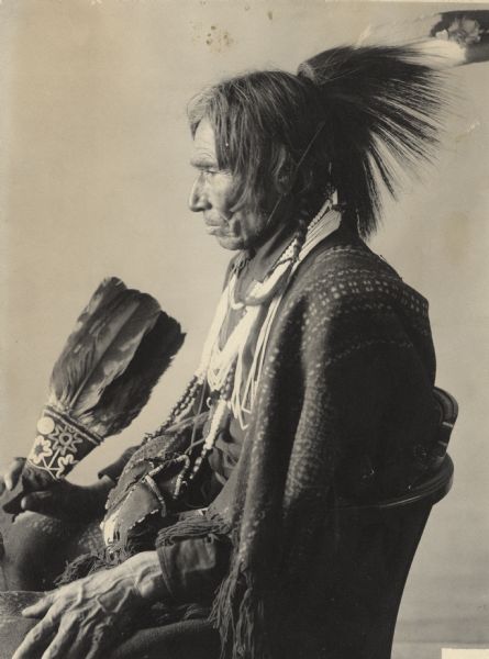 Studio portrait of Tabaiwatang or De-Bwawen-Dunk (Sound of Eating), called John, in partial native dress with ornaments and fan. Part of Algonquian and Chippewa Tribes.

