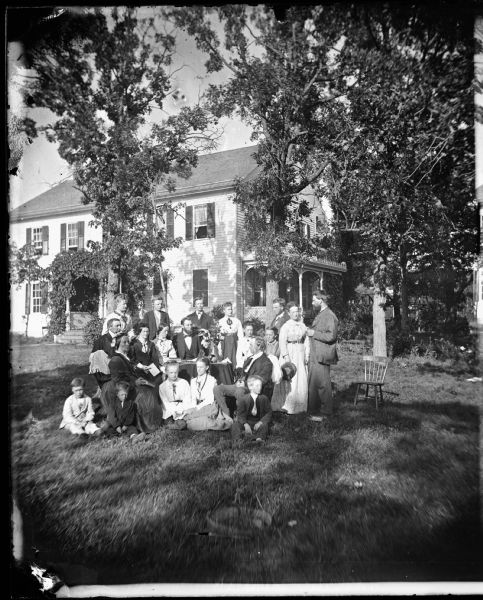 A gathering of ministerial families at the parsonage of Jacob Aaall Ottesen (1825-1904). Pastor Ottesen, seated on the far left with Mrs. Cathinka Doderlein Ottesen to his left, is visited by Pastor Herman Amberg Preus, his wife Caroline Keyser Preus and family. Visible also in this view are Jacob Magelssen, a medical doctor and son of a Lutheran minister in Rock County, Ottesen's son Otto, and Preus's son Christian Keyser. Preus and Ottesen were organizers of the Norwegian Lutheran Synod in Wisconsin in 1853. In anticipation of the 1867 synod meeting in Utica, Ottesen's congregation at Koshkonong built this two-story frame parsonage.