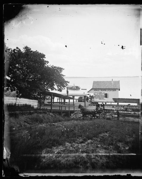 View from the foot of Carroll Street with the Angle Worm Station at Barnes boat landing on Lake Monona. Shows the <I>Scutt II</I> taken from the first successful steamboat, <I>Scutanawbequon</i>, launched July 21, 1864. There is an advertisement for Clark and Miller's general store featuring medicines, fancy goods and groceries.