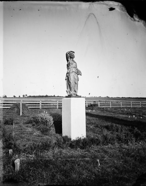 One of the eight female figures purchased from the Chicago firm Gould Brothers and Dribblee to be used on the gate posts of the Wisconsin State Capitol fence.  Only four were used and this is possibly the extra figure, "Candelabra." It became a memorial marker for Mary McFarland (died April 1, 1879) in the McFarland Family plot in McFarland Cemetery.