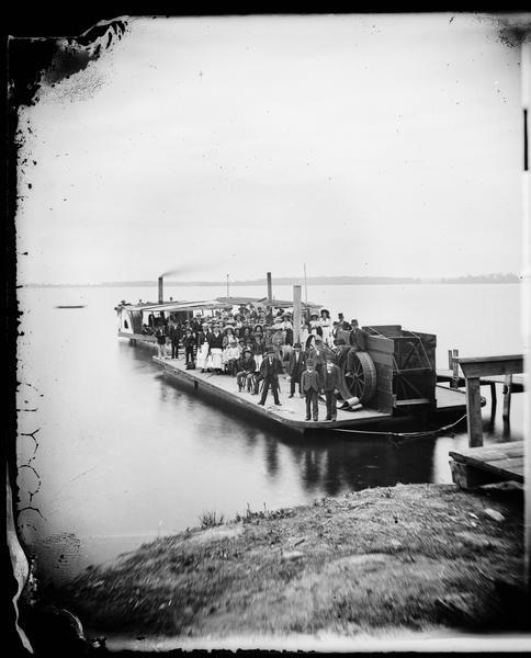 A large group of well-dressed people are standing aboard three small steamboats on Lake Monona. The boat in the foreground is a barge with a sternwheel. The two behind are sidewheel excursion boats.