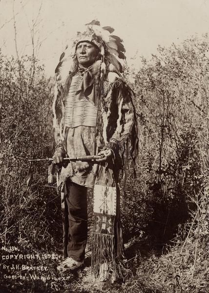 Full-length portrait of a Sioux man at the Rosebud Agency in full dress, ready for war.