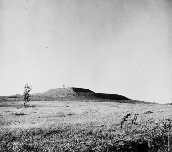 View of the southwest pyramidal mound in Aztalan State Park as it appeared after restoration.  A person is standing on top of the mound.