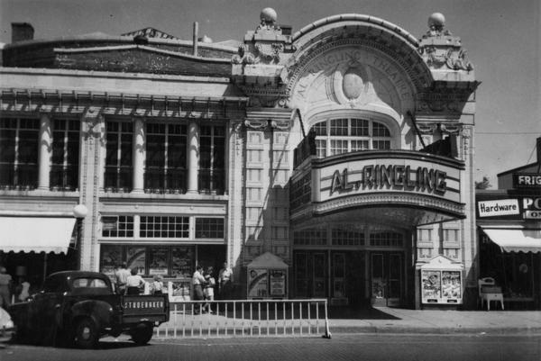 View across street of the Al. Ringling Theater with a Studebaker pickup truck in the foreground. There is a hardware store on the right.