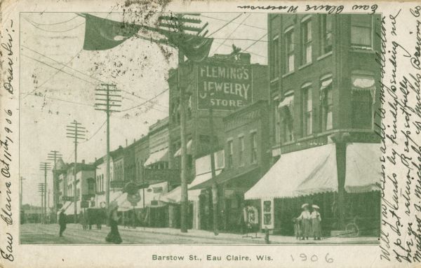 View of commercial buildings. One of the buildings has a sign painted on the side that reads: "Fleming's Jewelry Store." Several of the buildings have awnings hanging from them. A bicycle is on the lower right. Caption reads: "Barstow St., Eau Claire, Wis."