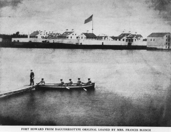 View of five soldiers rowing in a boat, beside a dock, with another soldier standing on the dock. The fort is in the background, complete with the fortified walls, and people standing in the front of the walls. The American flag stands above the fort in the center.