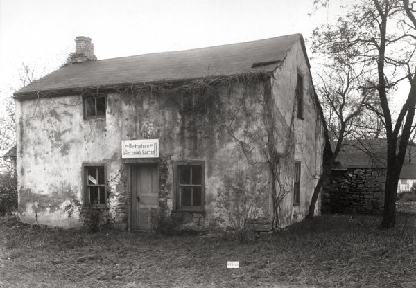 North elevation of the Jeremiah Curtin house, located at 8685 West Grange Avenue. This stone and stucco residence was erected in 1835. It has been recognized as the boyhood home of linguist and mythologist Jeremiah Curtin. A sign above the doorway reads: "Birthplace of Jeremiah Curtin".