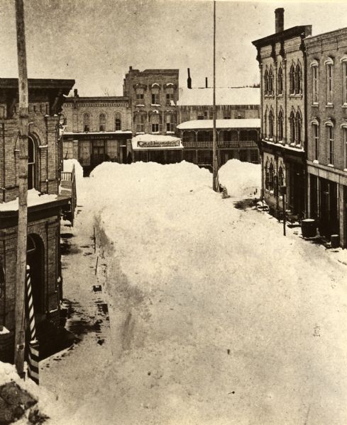 Winter scene looking north along First Street to its intersection with Main Street, Whitewater, Wisconsin. Shows aftermath of a big snowstorm which occurred between 27 Feb. and 3 March, 1881. According to the Whitewater Register newspaper "nothing like it was ever seen before in Wisconsin...". Photo was probably taken from the second story of the Bowers Opera House.