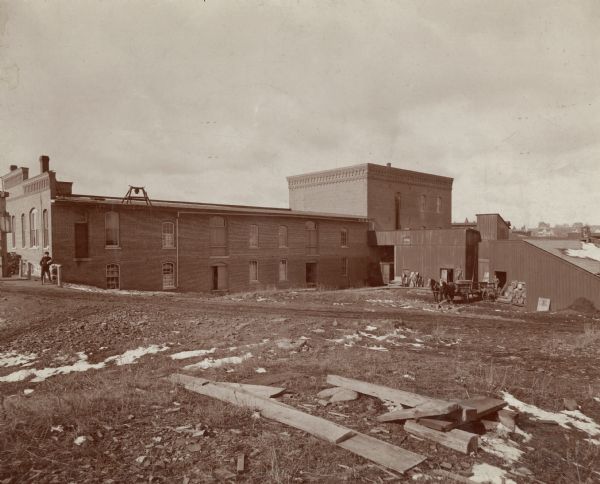 View of the Cereal Mills Company building, with men and a horse-drawn buggy outside on of the buildings on the right. Another man is standing on the far left.