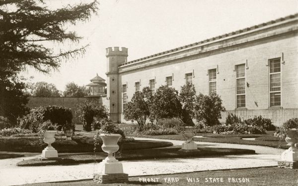 Caption reads: "Front Yard Wis State Prison." Landscaped yard with plants in urns on the lawn near a path in the foreground.