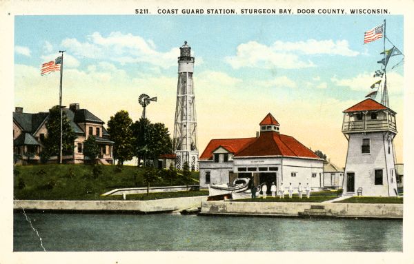 View of the coast guard station from the water with multiple sailors lined up near the shore. Caption reads: "Coast Guard Station, Sturgeon Bay, Door County, Wisconsin."