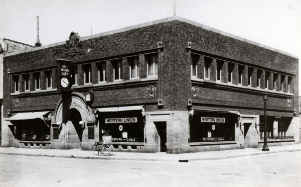 Exterior view of First National Bank. There are signs in the windows for Western Union.